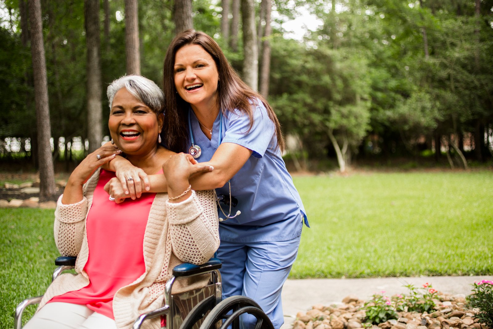 Wheelchair-bound African descent, female senior adult enjoys the outdoors with her home healthcare nurse or caregiver.  The multi-ethnic group is at the patient's home or a nursing home or assisted living facility.